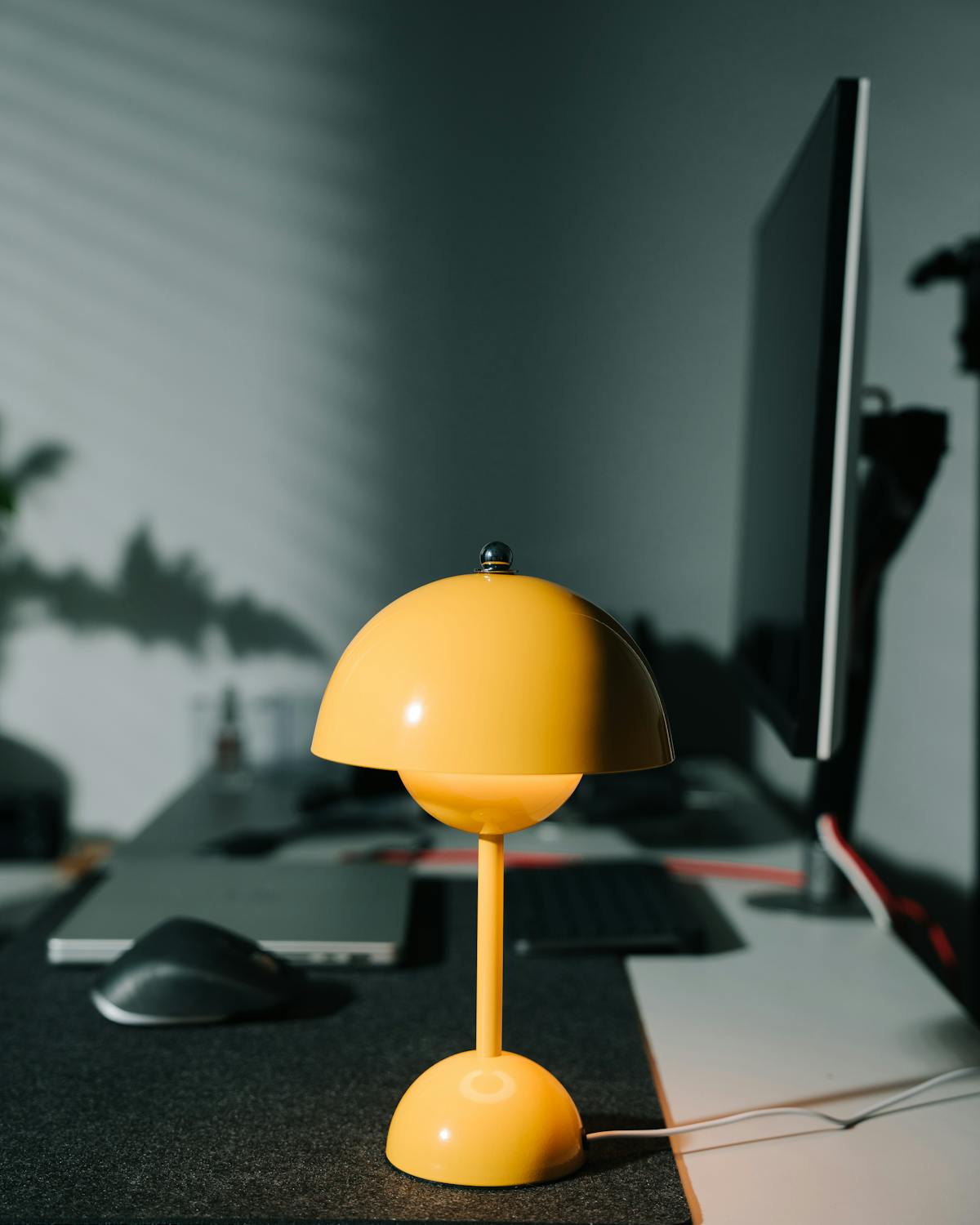 Minimal workspace with a mustard yellow desk lamp and dark monitor setup